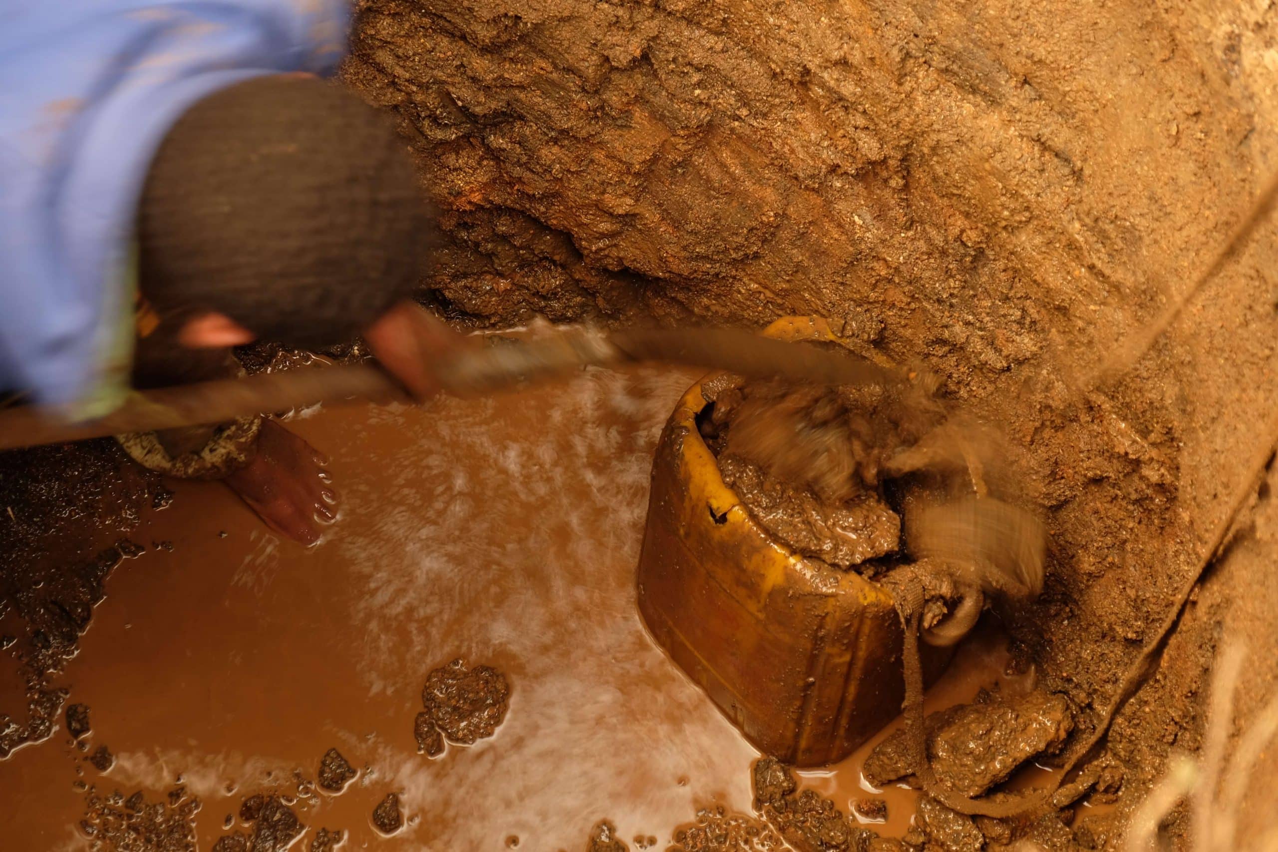 Man filling a bucket with soil from bottom of well